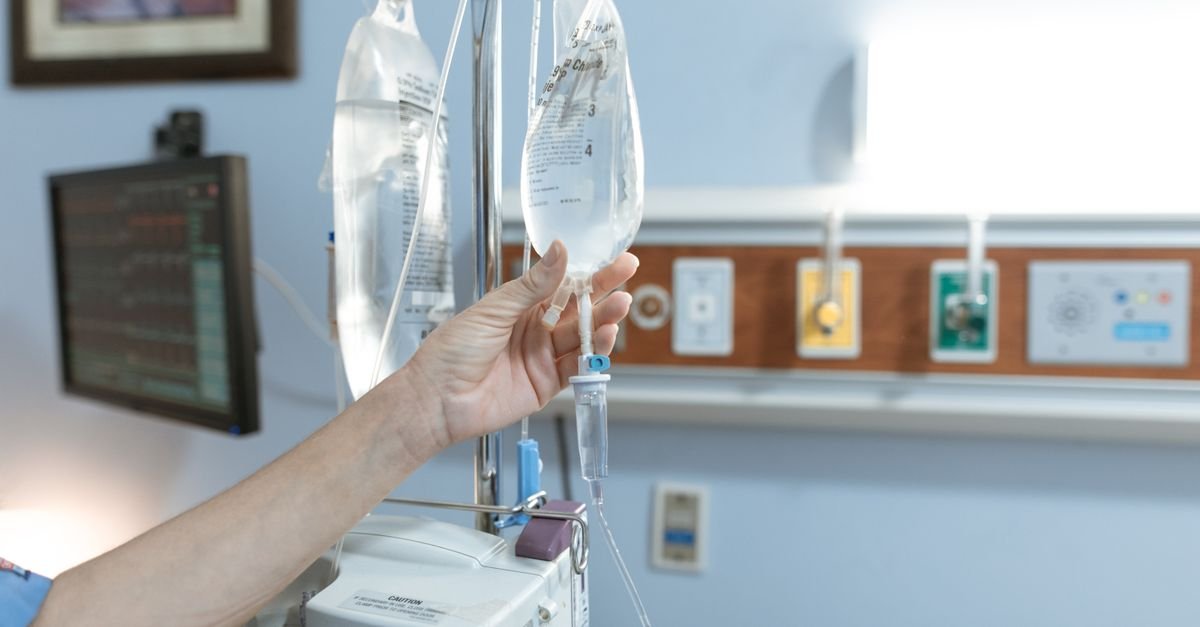 Close-up image of an IV drip and hand in a hospital room, illustrating medical care.