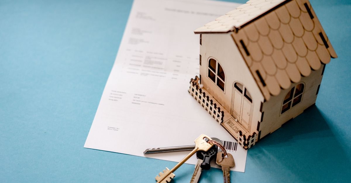 Miniature wooden house with keys and contract symbolizing real estate transactions.
