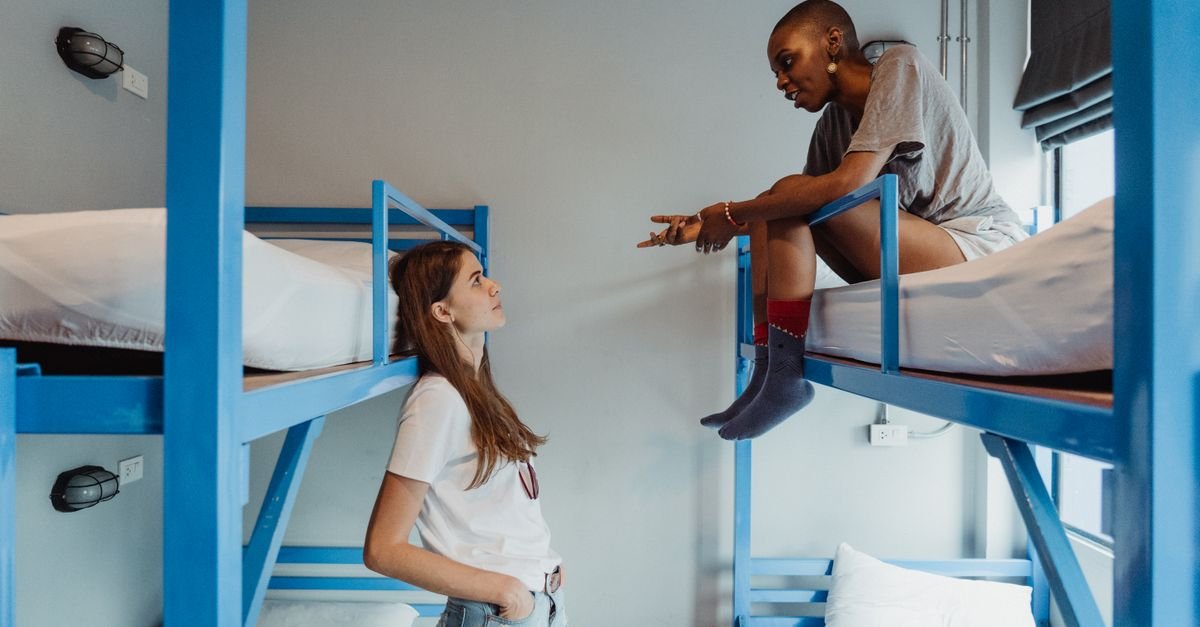 Two women engaging in conversation on bunk beds in a modern dormitory room.