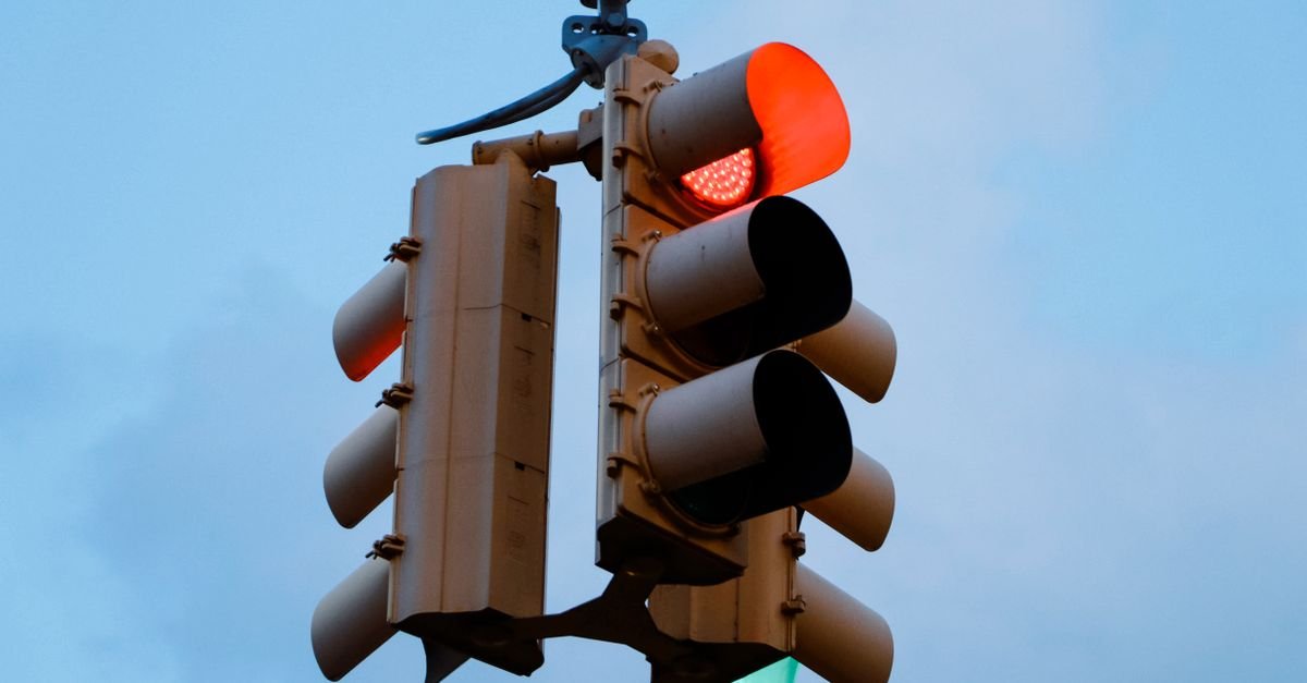 Close-up of a red traffic light signaling stop against a clear blue sky.