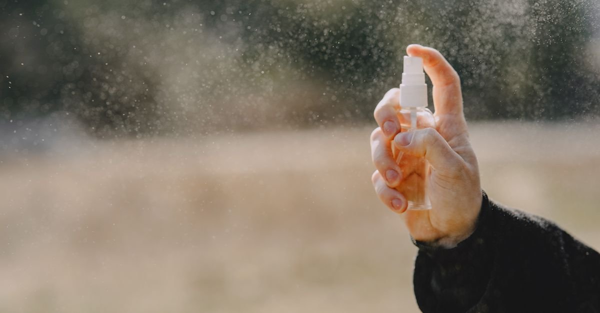 Unrecognizable man in casual wear showing bottle with liquid and spraying water outdoors