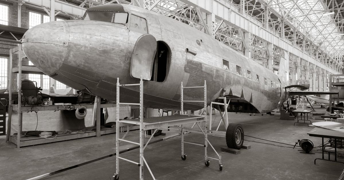 A classic aircraft undergoes restoration inside a spacious hangar, showcasing industrial architecture.