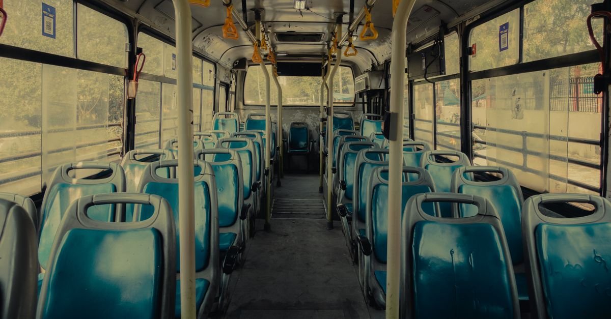 View of an empty public bus interior with blue seats and yellow handrails.