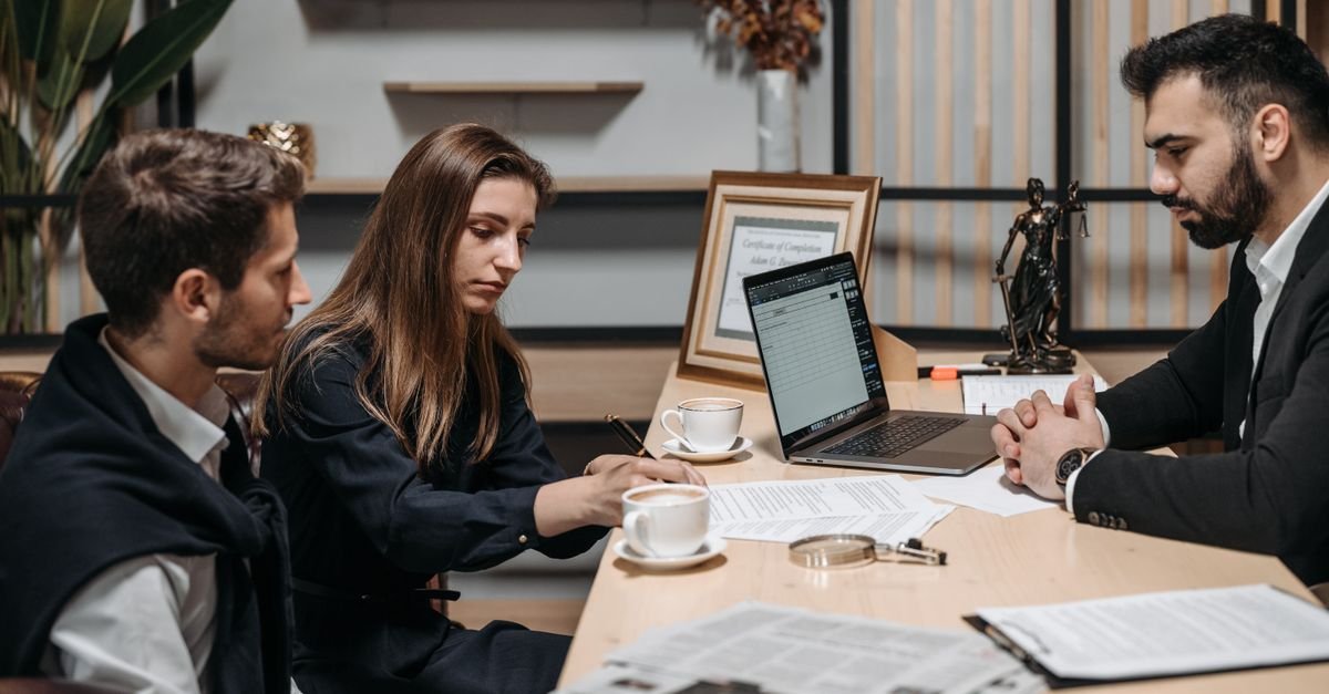 Three professionals discussing documents over coffee in a modern office setting.