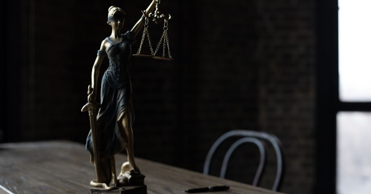 Lady Justice figurine on wooden table in dimly lit room symbolizes law and fairness.