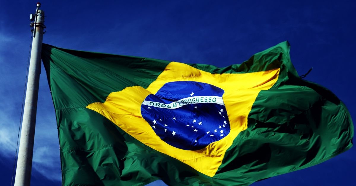 A dynamic shot of the Brazilian flag waving on a flagpole with a clear blue sky background.