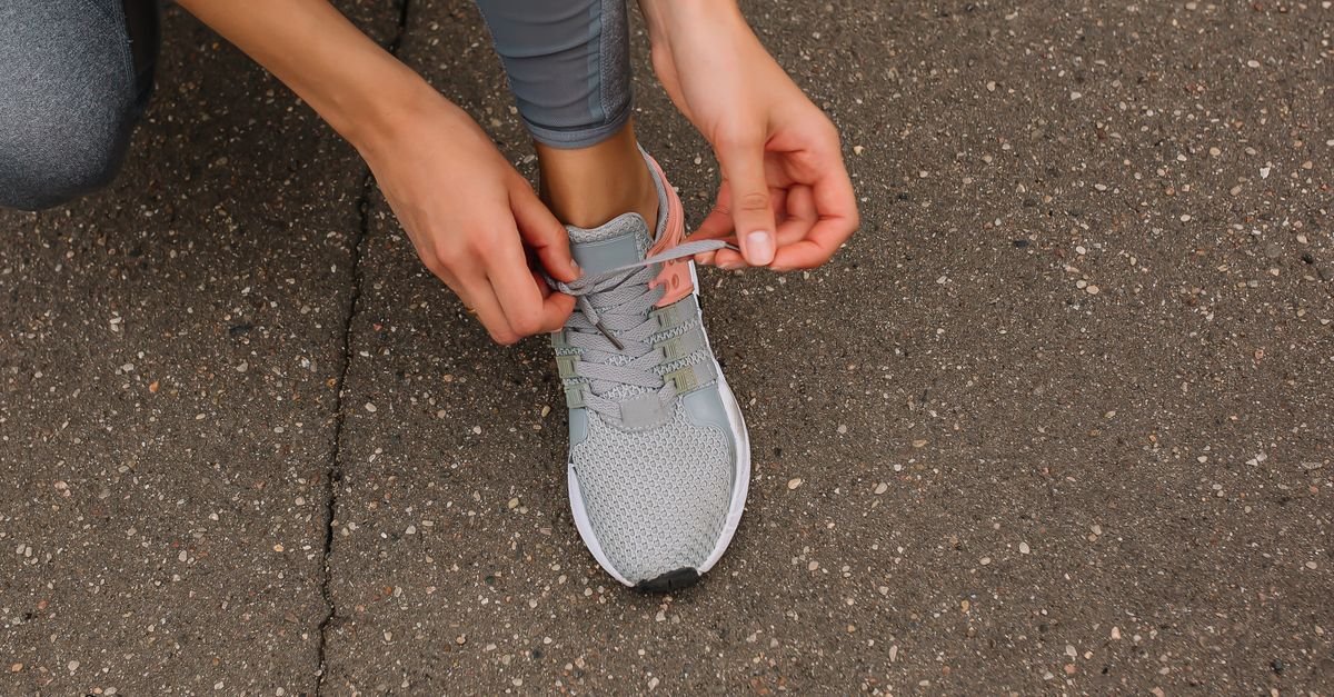 Close-up image of a person tying shoelaces on a sneaker while sitting on pavement.