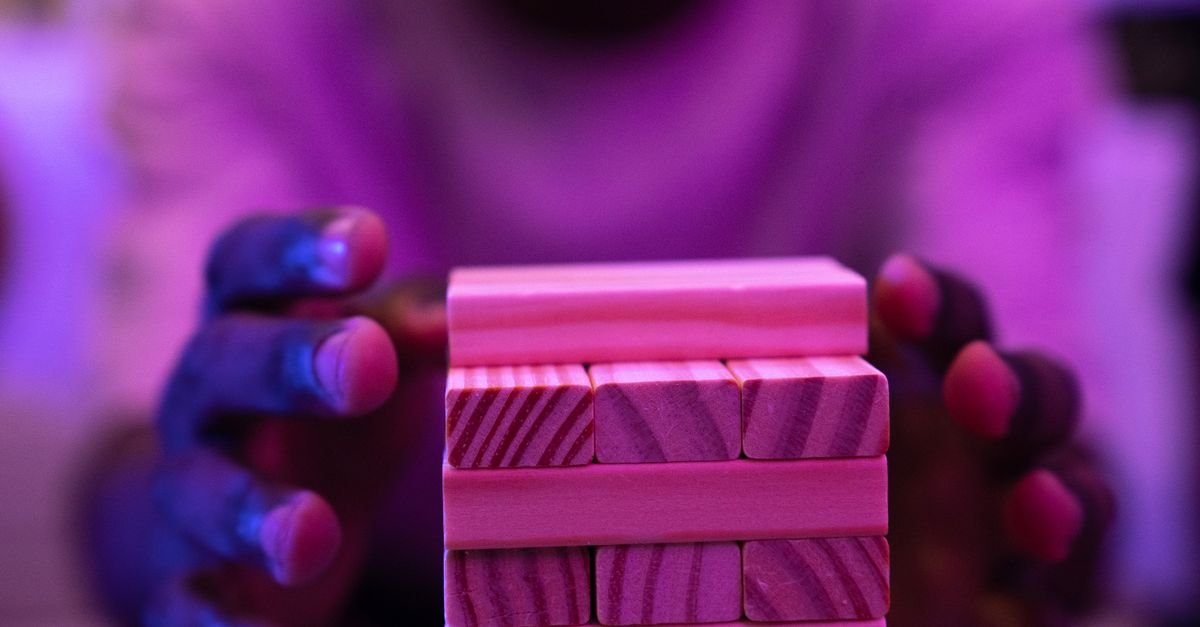 A vibrant close-up capture of hands stacking wooden blocks in a game setting under neon lighting.