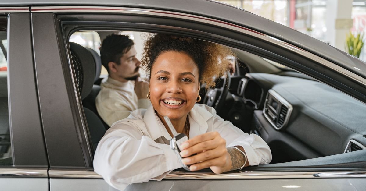 Joyful couple in their new car, holding keys in a dealership showroom, smiling warmly.