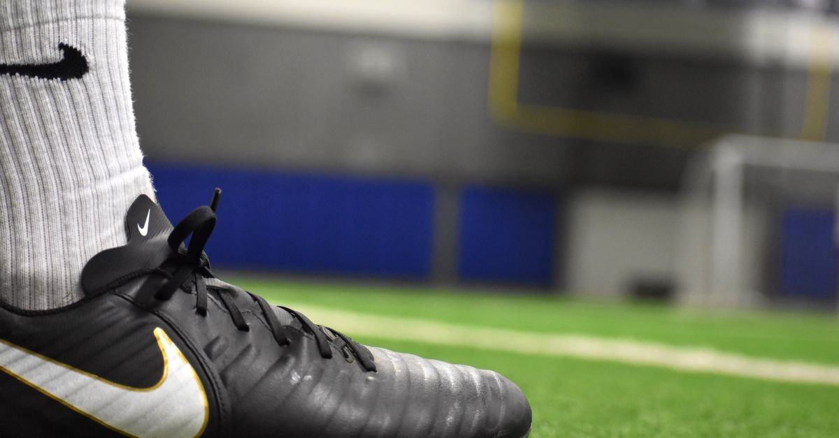 A detailed shot of a soccer cleat on an indoor turf field, emphasizing footwear and athletic activity.
