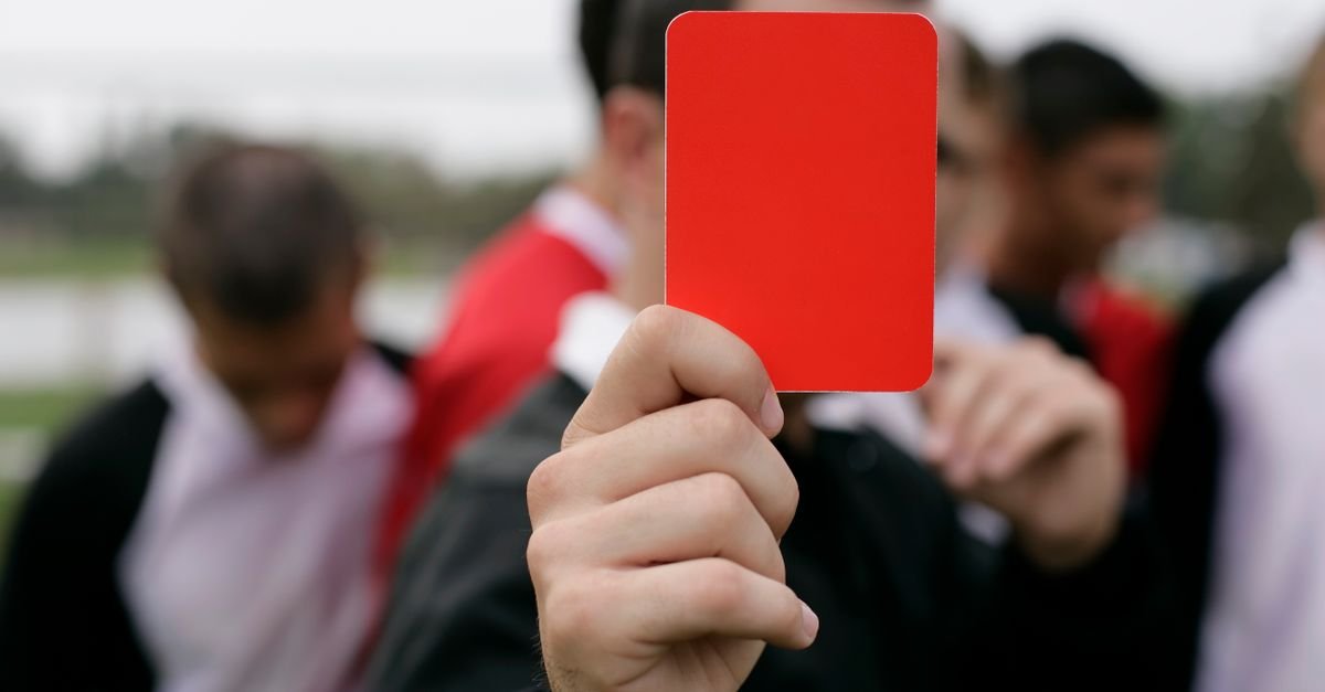 Referee showing a red card to players during an outdoor soccer game.