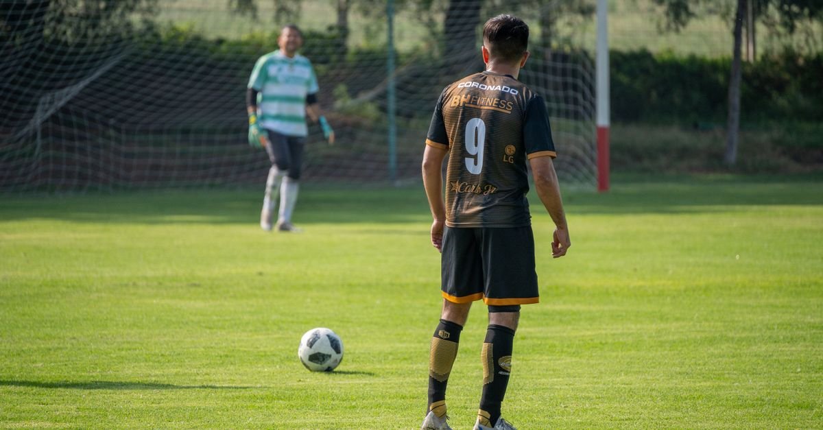 Soccer player in action preparing for a penalty kick on a sunny day in a green field.