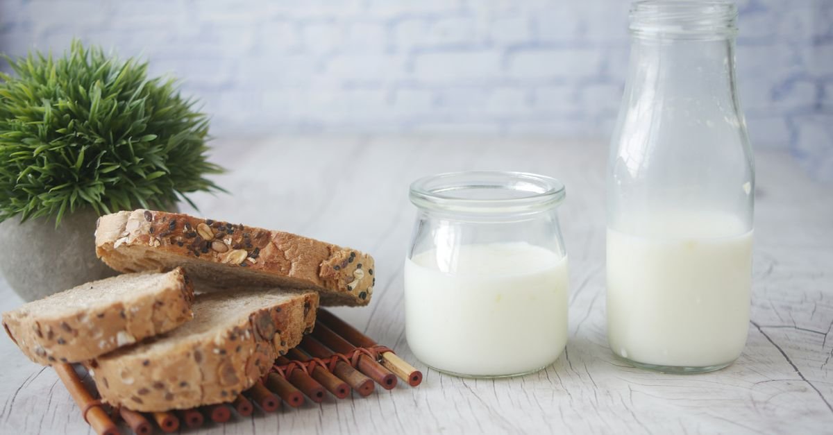 Slices of multigrain bread with a bottle and jar of milk on a wooden table.