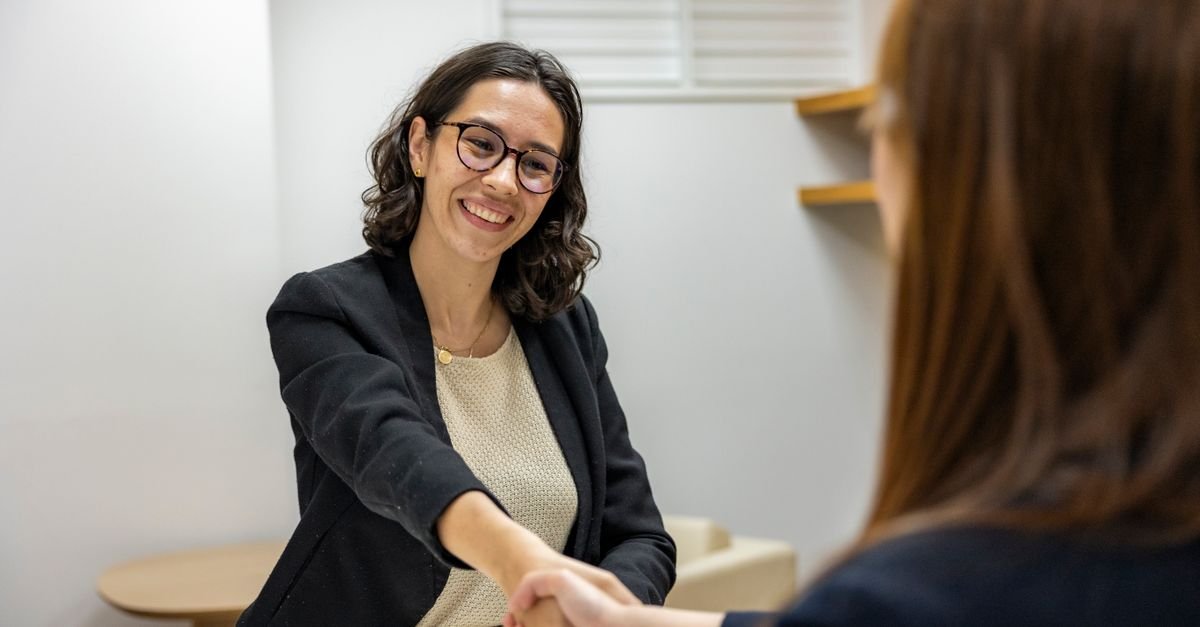 Businesswomen shaking hands in an office, representing a successful job interview or partnership.