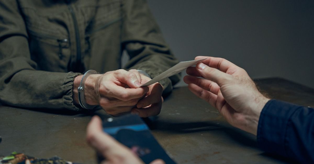 Hands exchanging evidence during an interrogation scene in a dimly lit room.