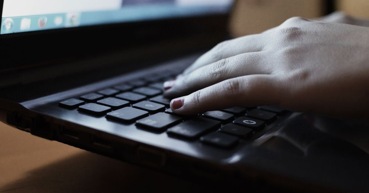 A close-up view of a person typing on a laptop keyboard indoors.