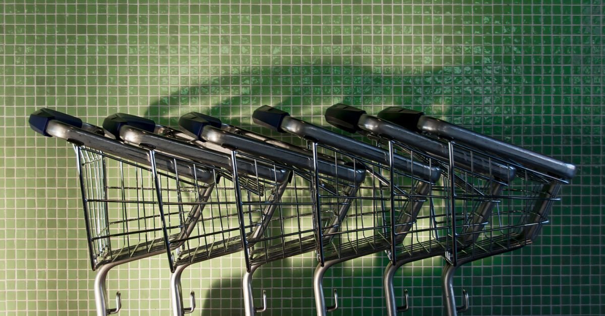 A row of neatly arranged shopping carts in front of a green tiled wall with shadows.