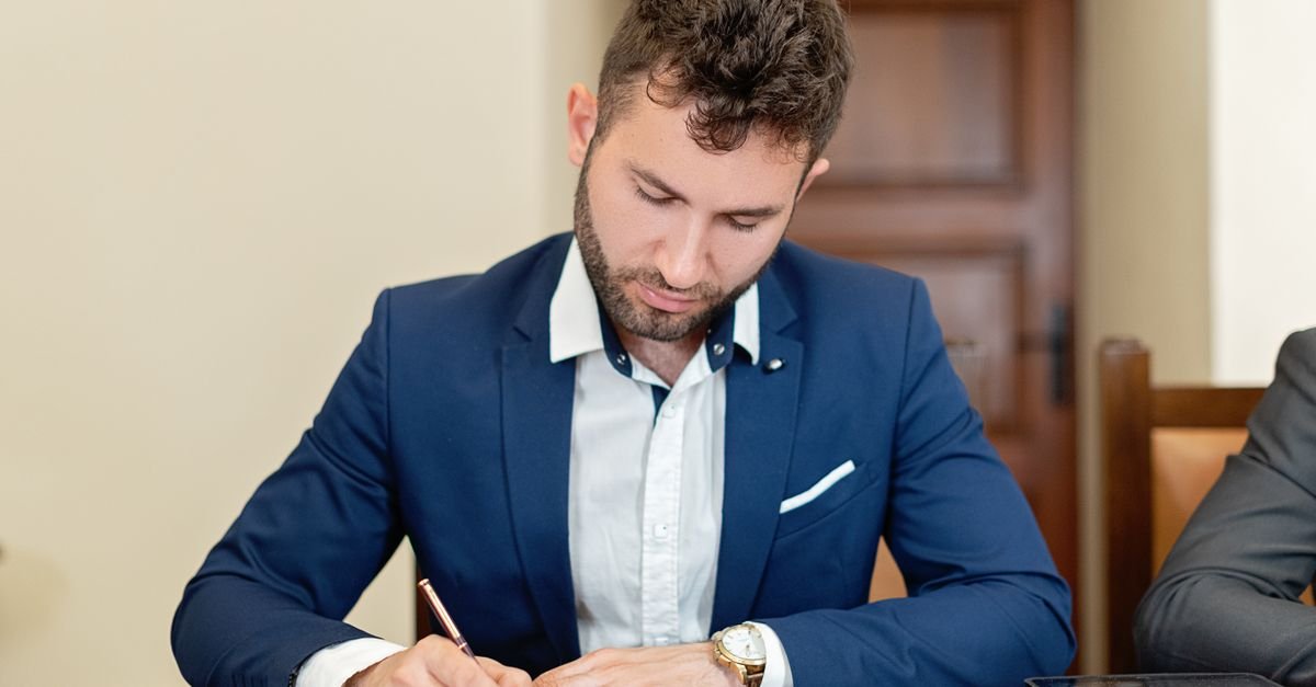 Confident businessman in a suit signing a contract at the office desk.