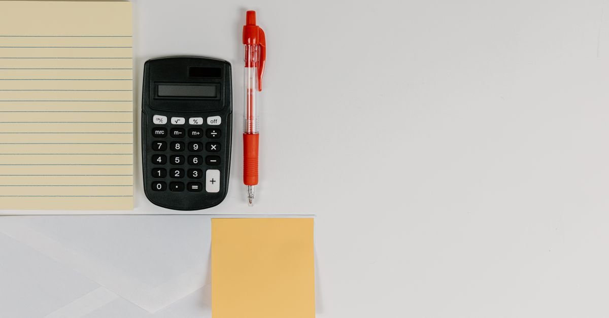 Top view of calculator, pen, and note pads arranged neatly on a white surface.