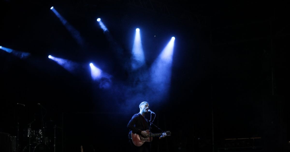 Solo musician performs on stage with guitar under dramatic blue lighting during a live concert.