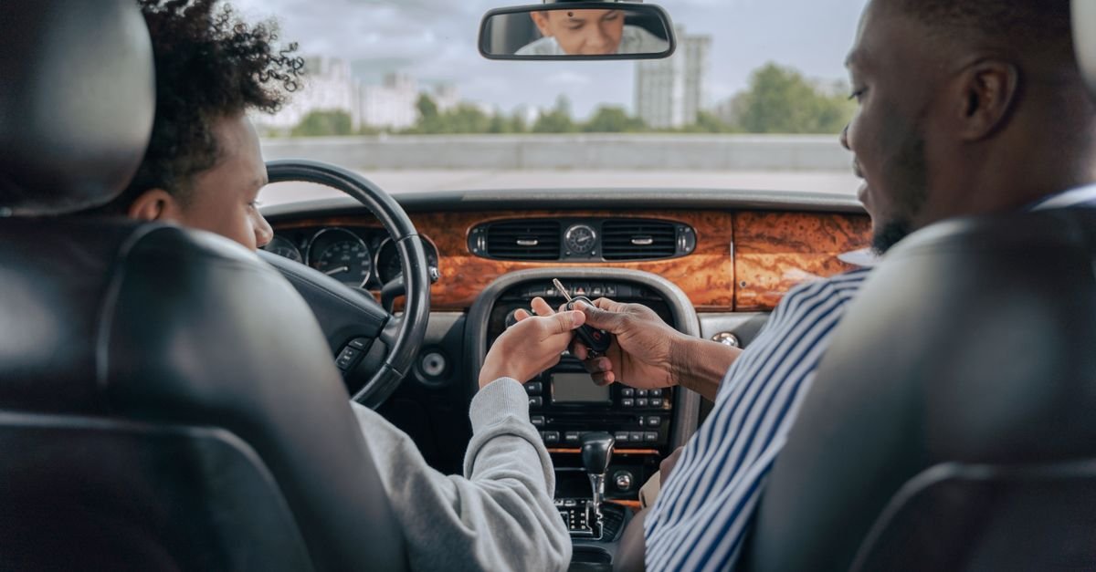 Father and teenage son inside car learning to drive, fostering bonding and guidance.