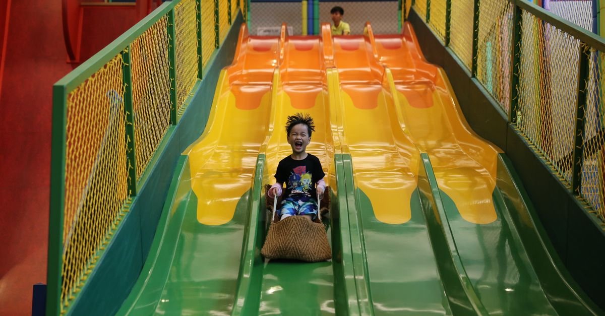 A cheerful child sliding down a colorful slide in an indoor playground, showcasing fun and excitement.