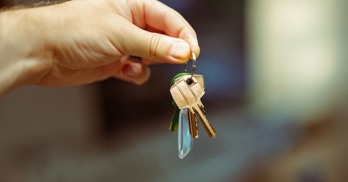 A close-up image of a hand holding a keyring with several house keys, symbolizing real estate and home ownership.