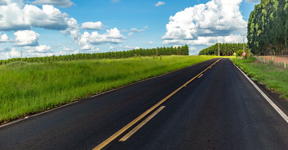 A scenic road leading through a lush green countryside under a blue sky with fluffy clouds.