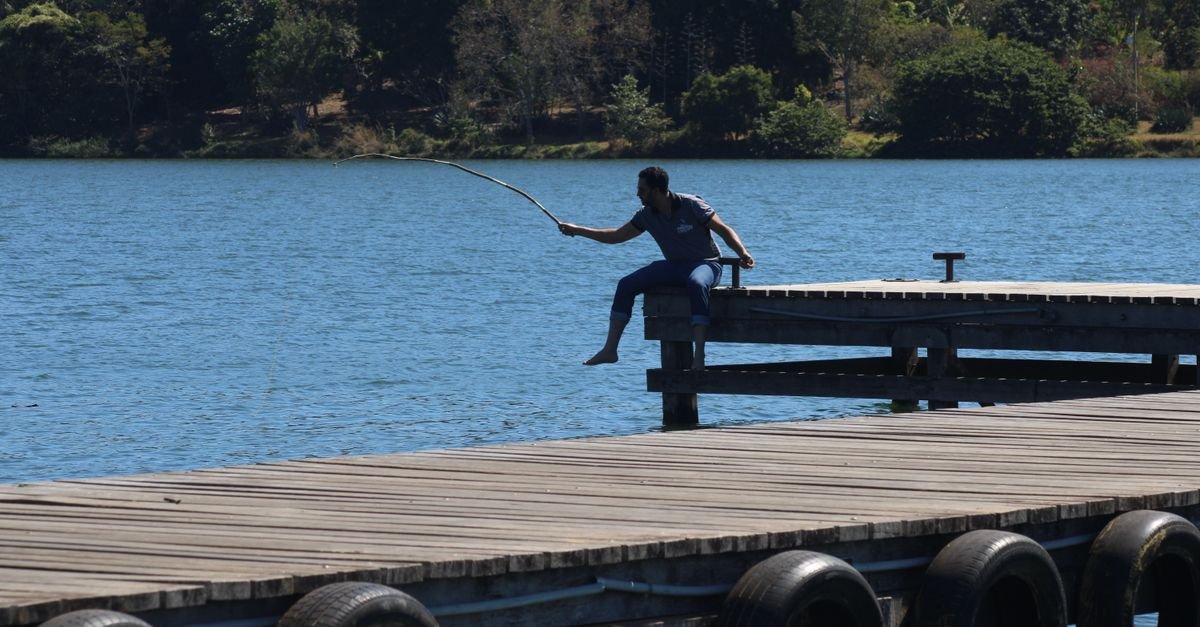 Adult man fishing from a wooden pier on a sunny day at a lake in Brasília, Brazil.