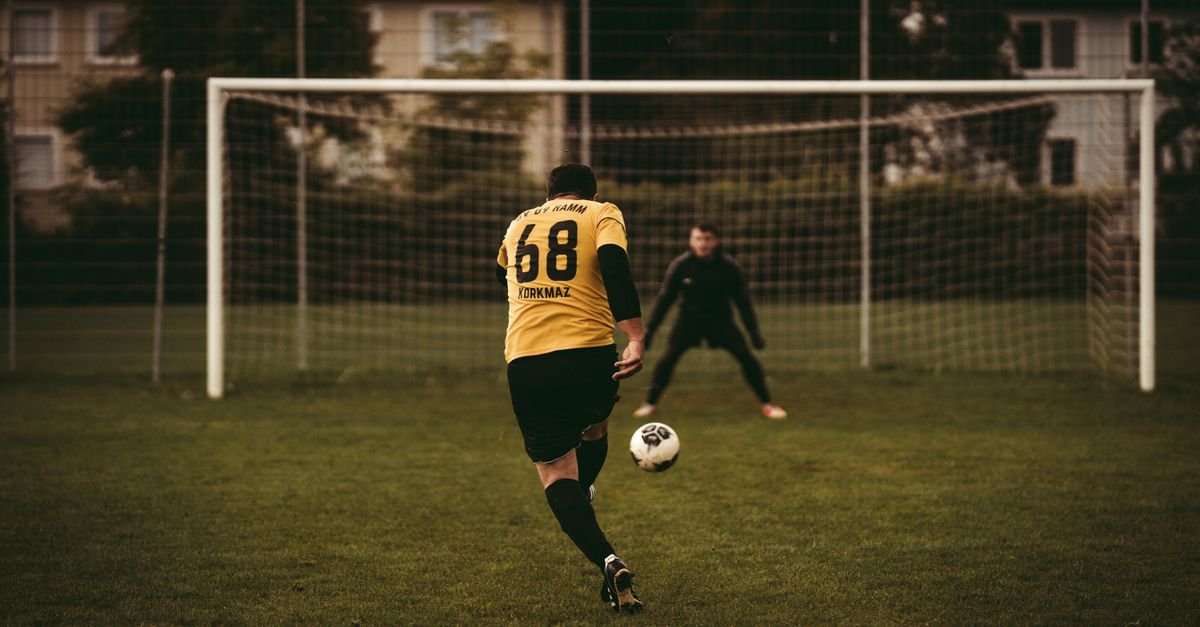 A soccer player takes a decisive penalty kick aiming to score against the goalkeeper.