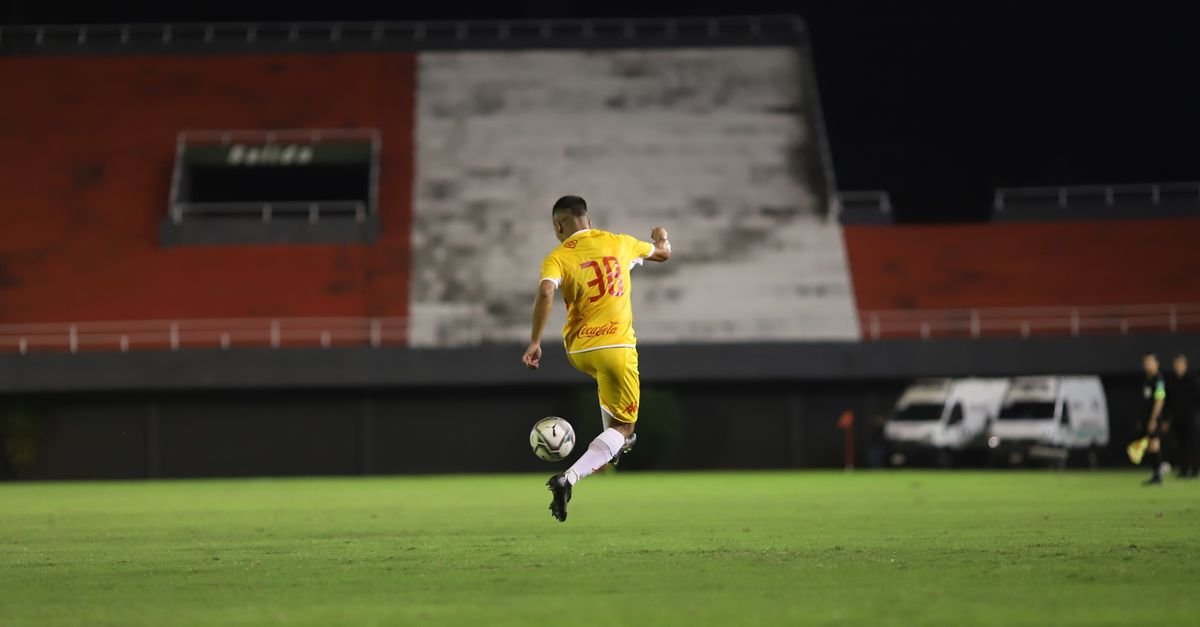 Soccer player in yellow jersey kicking a ball on a green pitch during night match under lights.