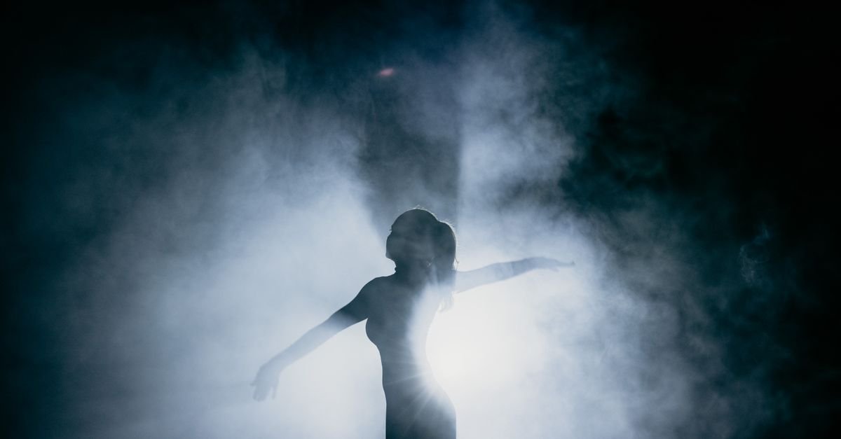 Captivating silhouette of a dancer gracefully posing amidst smoke, illuminated by dramatic backlight.