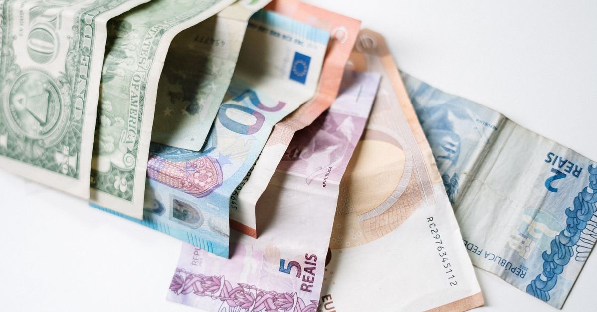 A collection of different international currency notes, including US Dollar, Euro, and Brazilian Real, on a white background.