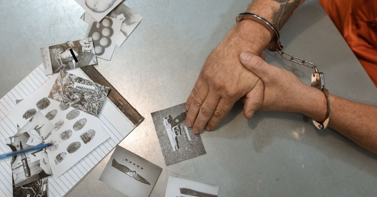 A handcuffed individual examines evidence photos and documents during an investigation.