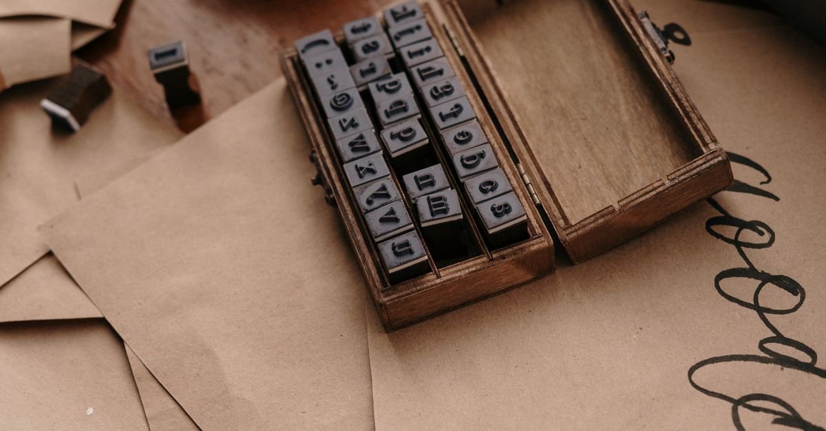 Vintage wooden box containing rubber alphabet stamps on brown paper envelopes.