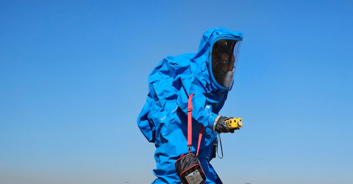 Protective hazmat suit worn by individual inspecting outdoors during daylight.
