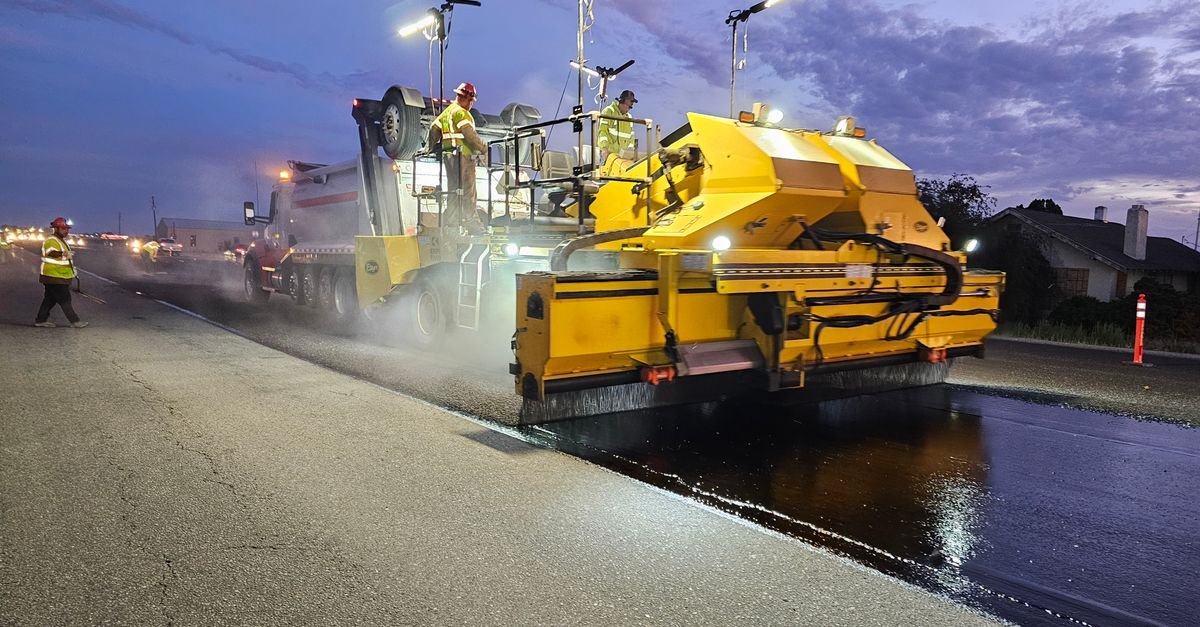 Workers operate heavy machinery to pave a road at twilight, enhancing infrastructure.