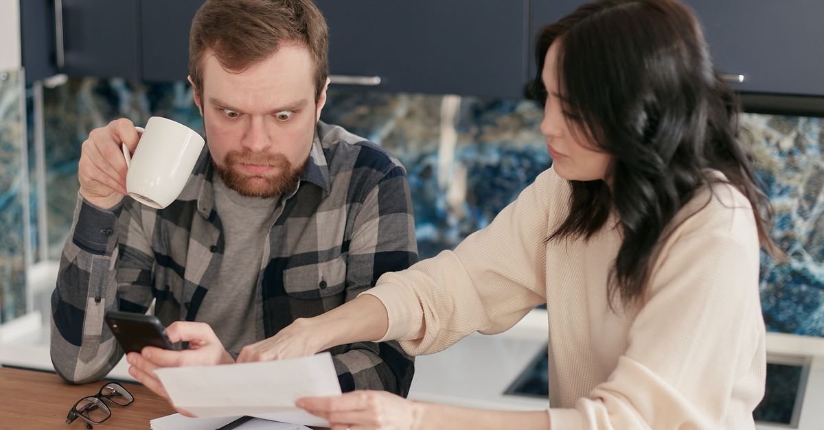 A couple reviews household bills in a kitchen, appearing concerned and focused.