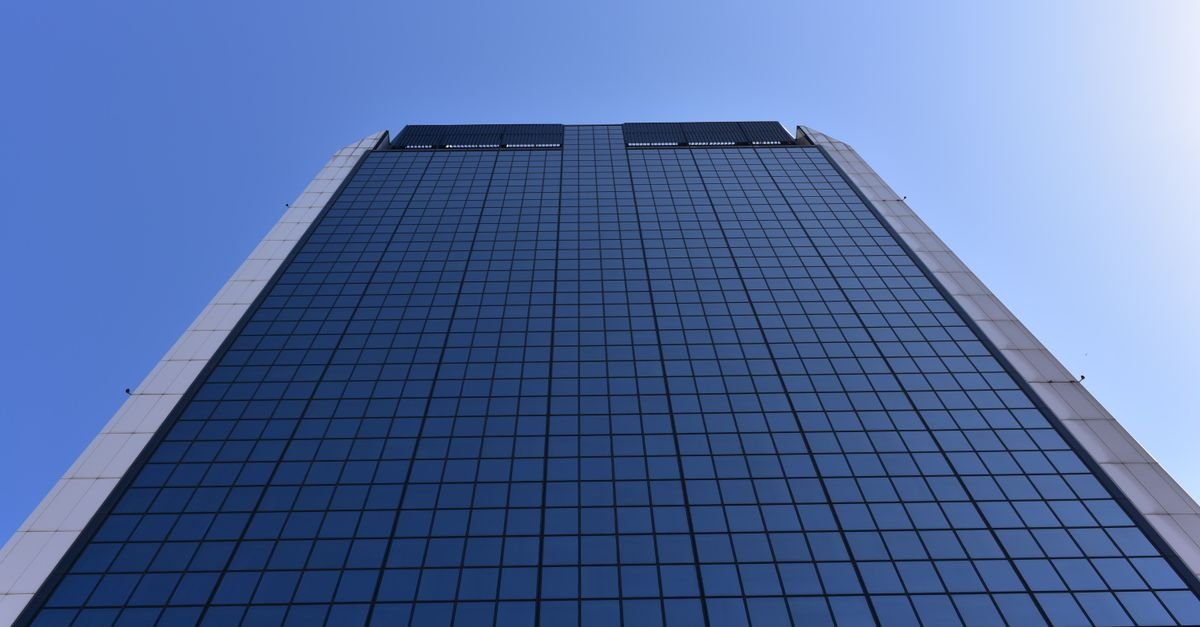 Low-angle shot of a tall glass skyscraper against a clear blue sky, showcasing modern architecture.