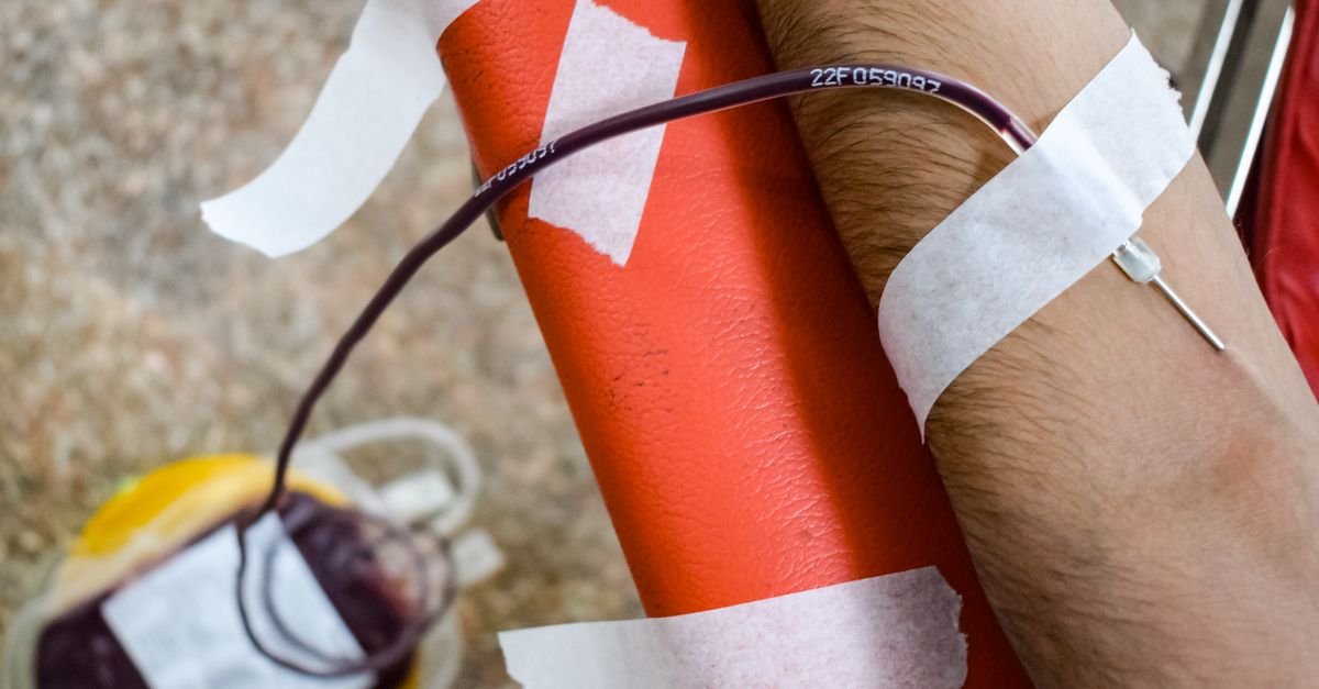 Detailed view of arm during blood donation, highlighting needle insertion and blood bag.