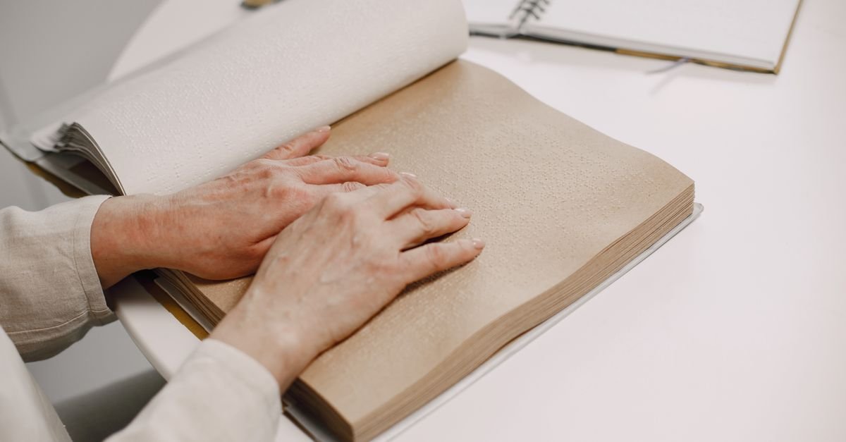 Mãos de uma pessoa lendo um livro impresso em braille sobre uma mesa