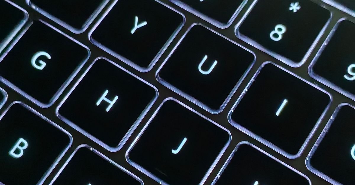 Close-up de teclado de notebook com teclas retroiluminadas em ambiente escuro