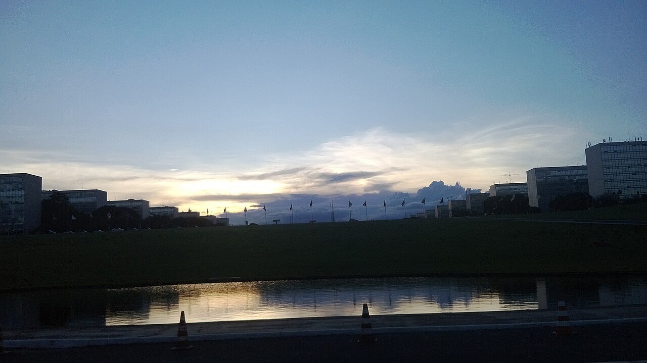 Esplanada dos Ministérios em Brasília ao entardecer, com os prédios e as bandeiras em contraluz