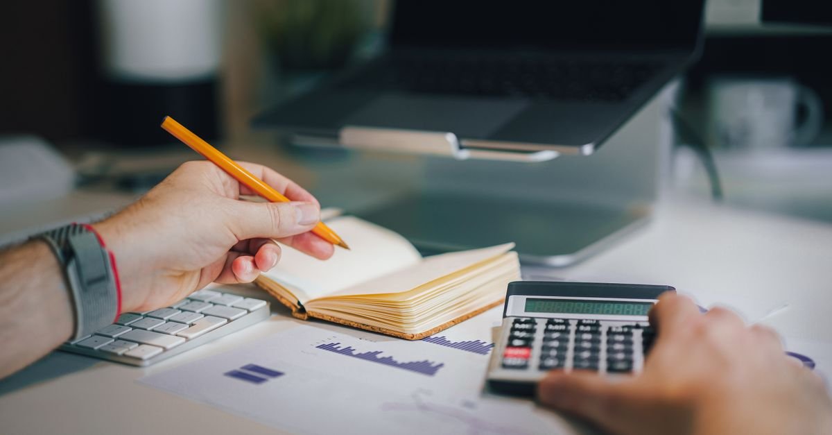 Mãos de pessoa usando calculadora sobre planilha com gráficos financeiros
