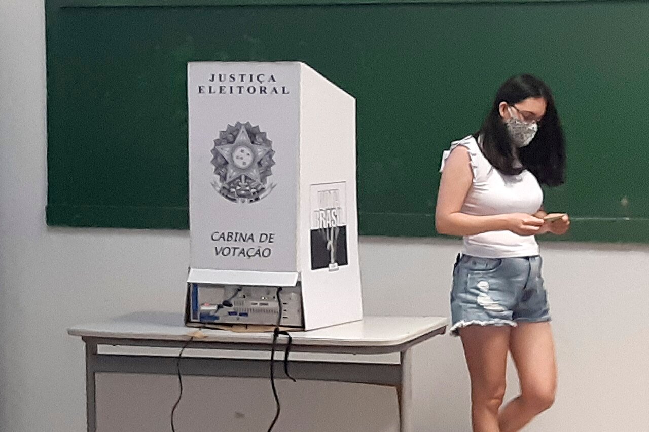 Eleitora deixa a cabine de votação da Justiça Eleitoral ao lado da urna eletrônica em seção eleitoral