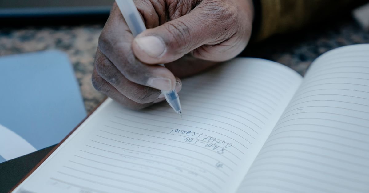 Mão segurando caneta e escrevendo em caderno pautado