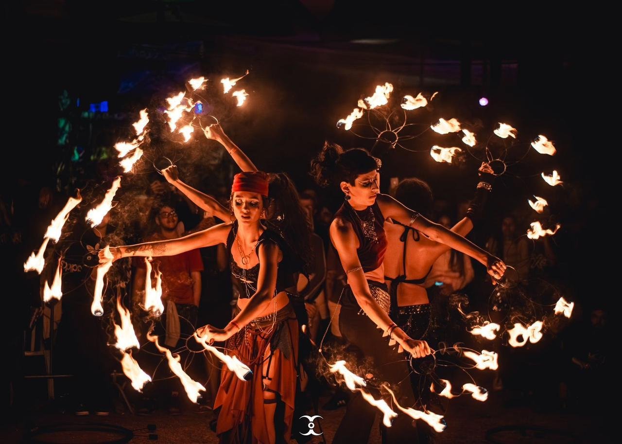 Duas artistas circenses giram aparelhos de fogo durante apresentação noturna ao ar livre
