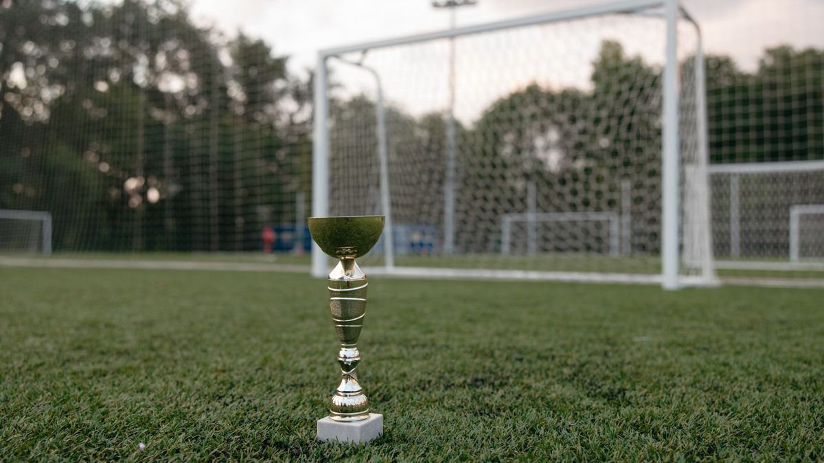 Troféu dourado sobre o gramado em frente a um gol de futebol