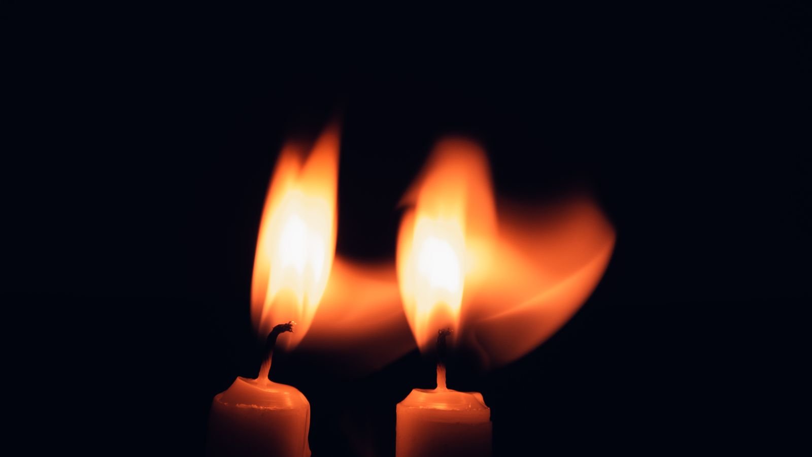Duas velas acesas contra fundo escuro