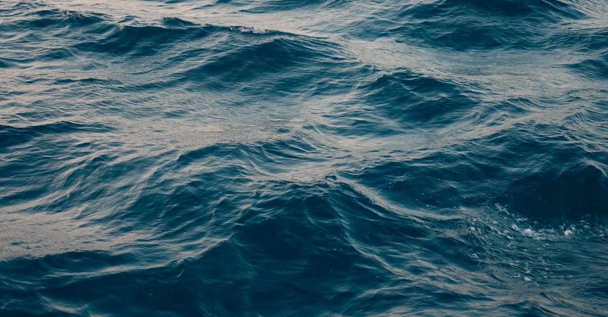 Superfície do mar aberto em tom azul escuro, com ondulação, vista de cima